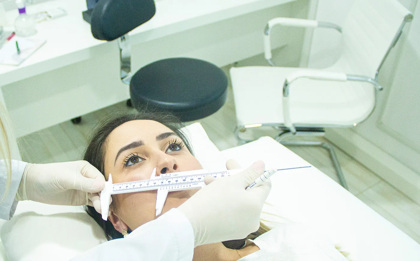 Avaliação facial na clínica: profissional de luvas mede o rosto da paciente com uma régua
